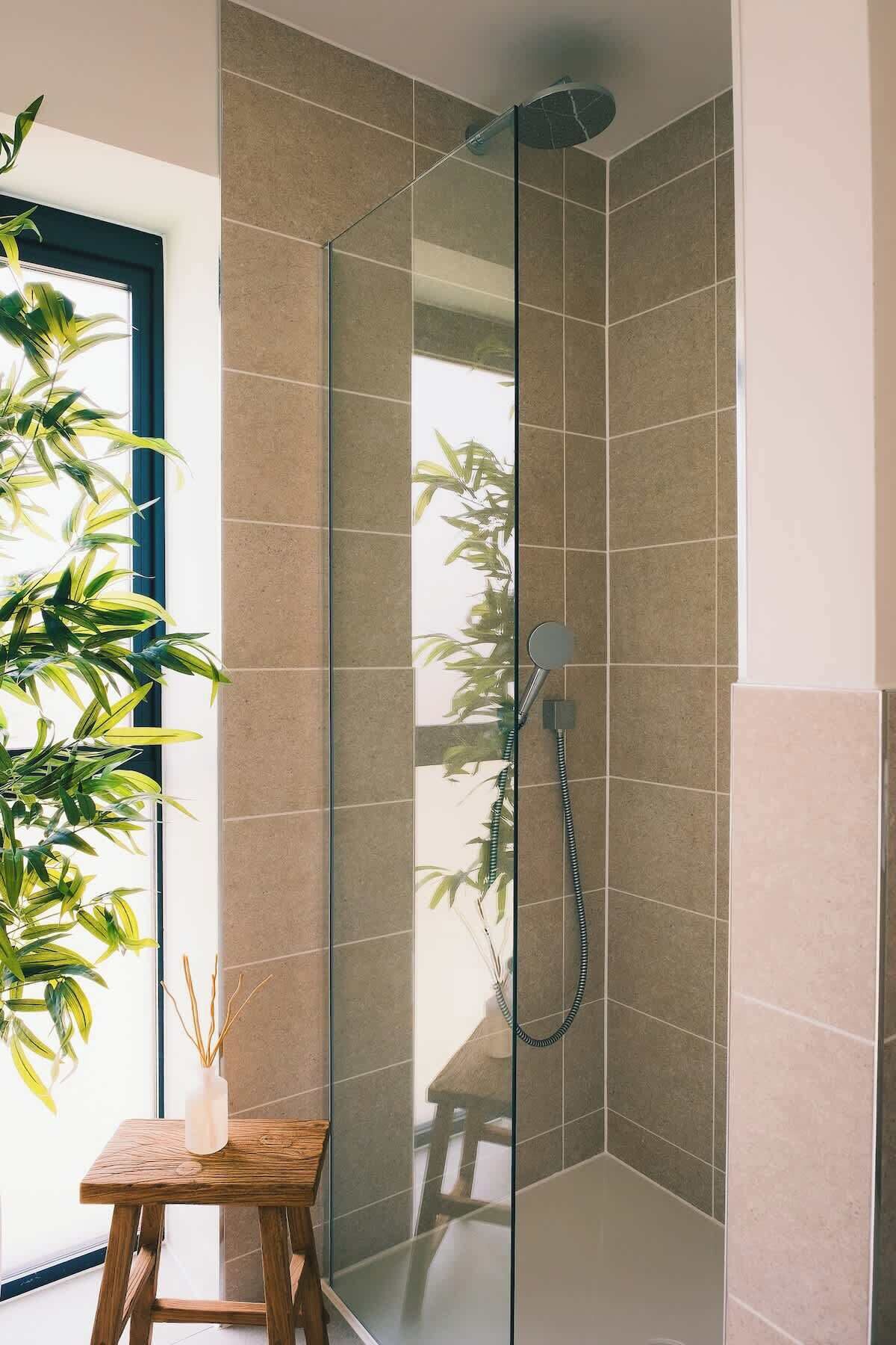 Een moderne douche met een glazen deur, gebetongrijs tegels en een handdouche.
