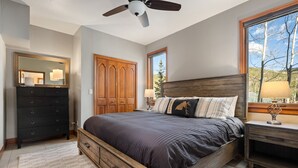 A bedroom with a wooden bed, a dresser, a wardrobe, and a window with a view of trees. - Ski Inn Condo 1 Bedroom Condo (Winter Park)