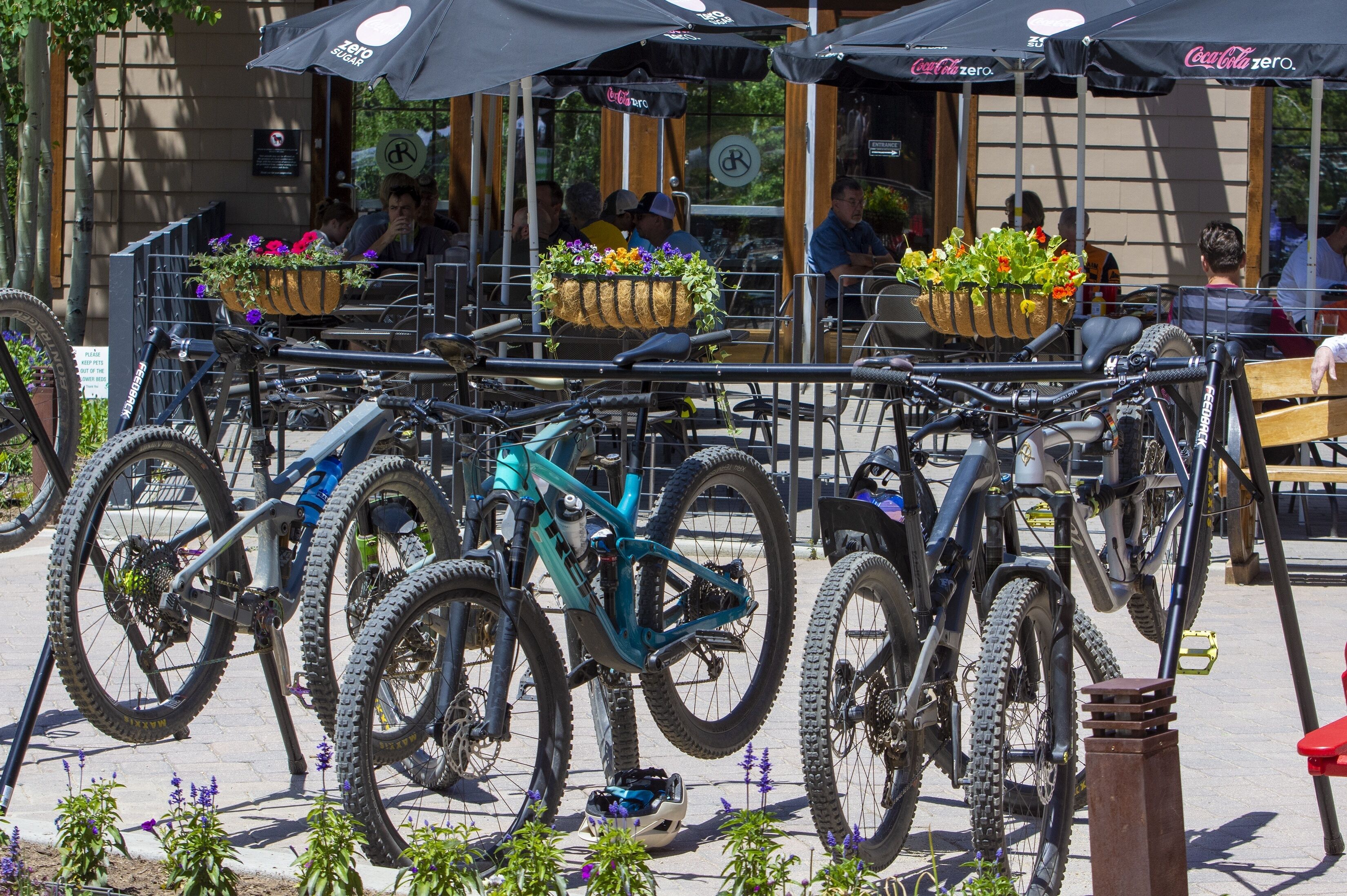 A row of bicycles parked in front of outdoor seating areas with tables and umbrellas.