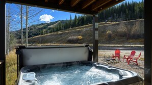 A hot tub with a view of a forested hillside and a gravel area with red chairs. - Ski Inn Condo 1 Bedroom Condo (Winter Park)