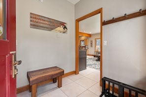 A hallway with a wooden bench, a door with a red frame, a wall-mounted sign, and a mirror reflecting a kitchen area. - Ski Inn Condo 1 Bedroom Condo (Winter Park)