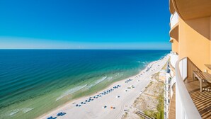 Une vue sur la plage depuis un balcon, avec une eau d’un bleu limpide, une plage de sable et des parasols.
