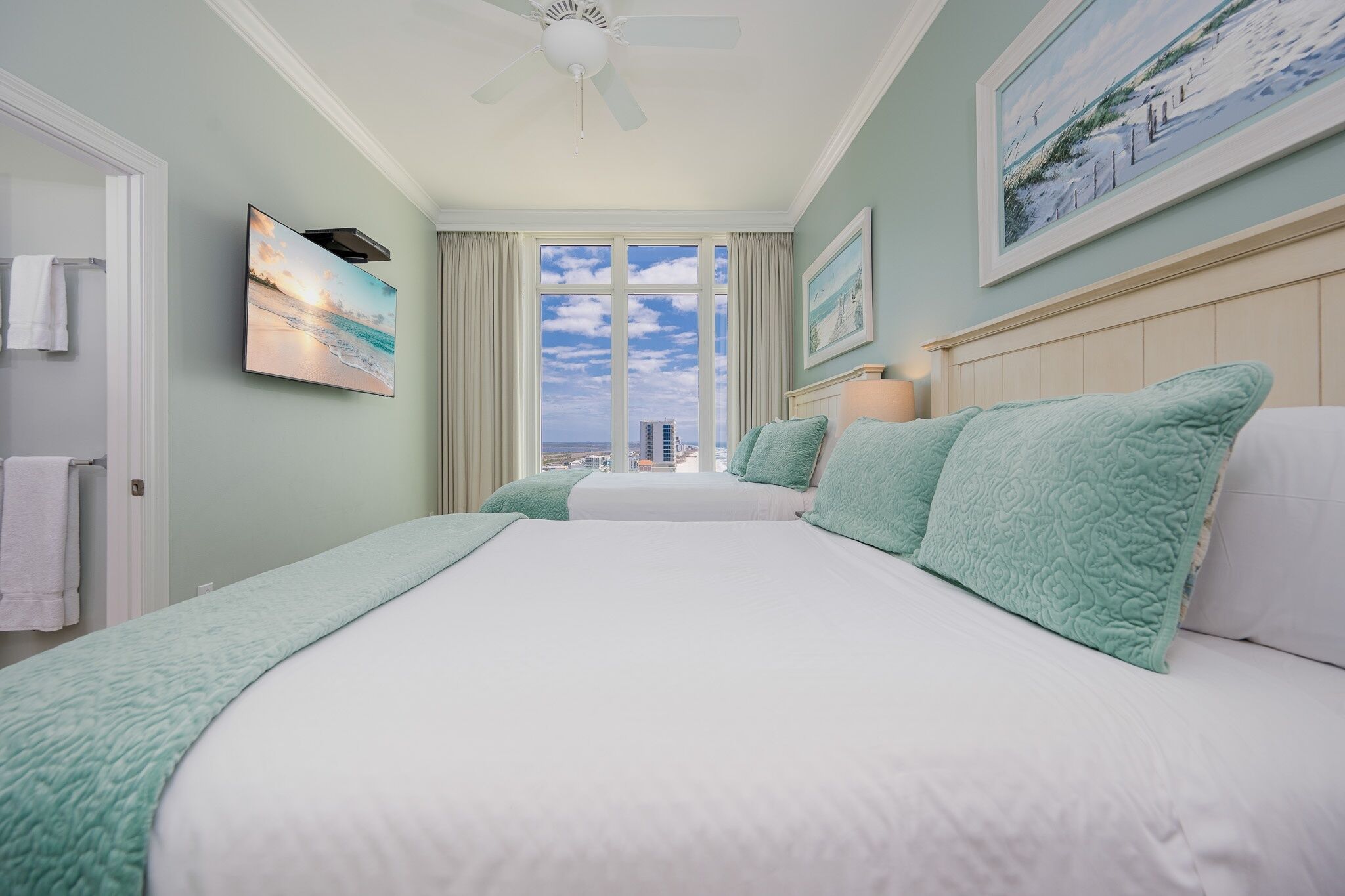 Camera da letto con un letto grande, una ventola a soffitto, un quadro e vista sulla città dalla finestra.