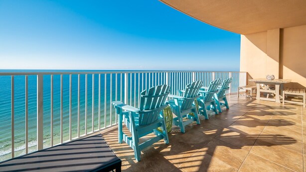 Un balcon avec des fauteuils Adirondack turquoise, une petite table et une vue sur l’océan.