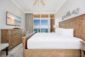A hotel room with a large bed, wooden headboard, a flat-screen TV, a dresser, and a view of the ocean. - Phoenix Gulf Shores by Brett/Robinson Vacations (Gulf Shores)