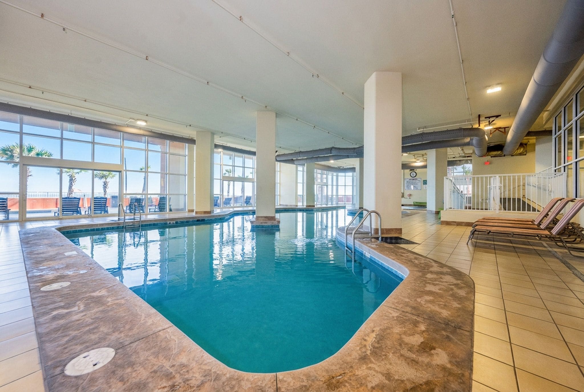 An indoor swimming pool with clear blue water, surrounded by lounge chairs and a tiled floor.