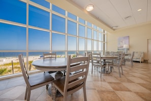 A dining area with large windows overlooking a beach, featuring round tables and wooden chairs. - Phoenix Gulf Shores by Brett/Robinson Vacations (Gulf Shores)