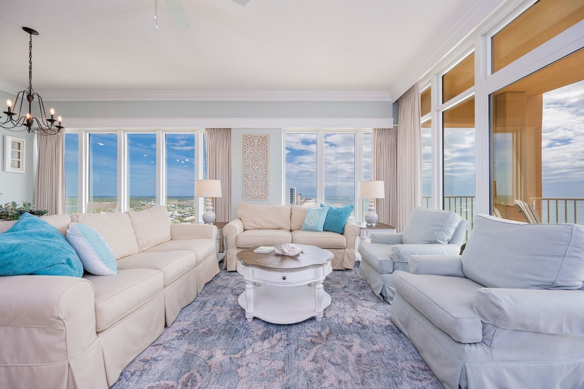 A spacious living room with a large window, a chandelier, and a white coffee table.
