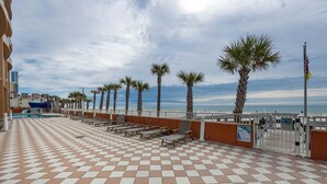 Un espace extérieur à carreaux, agrémenté de bancs, de palmiers et offrant une vue sur l’océan.