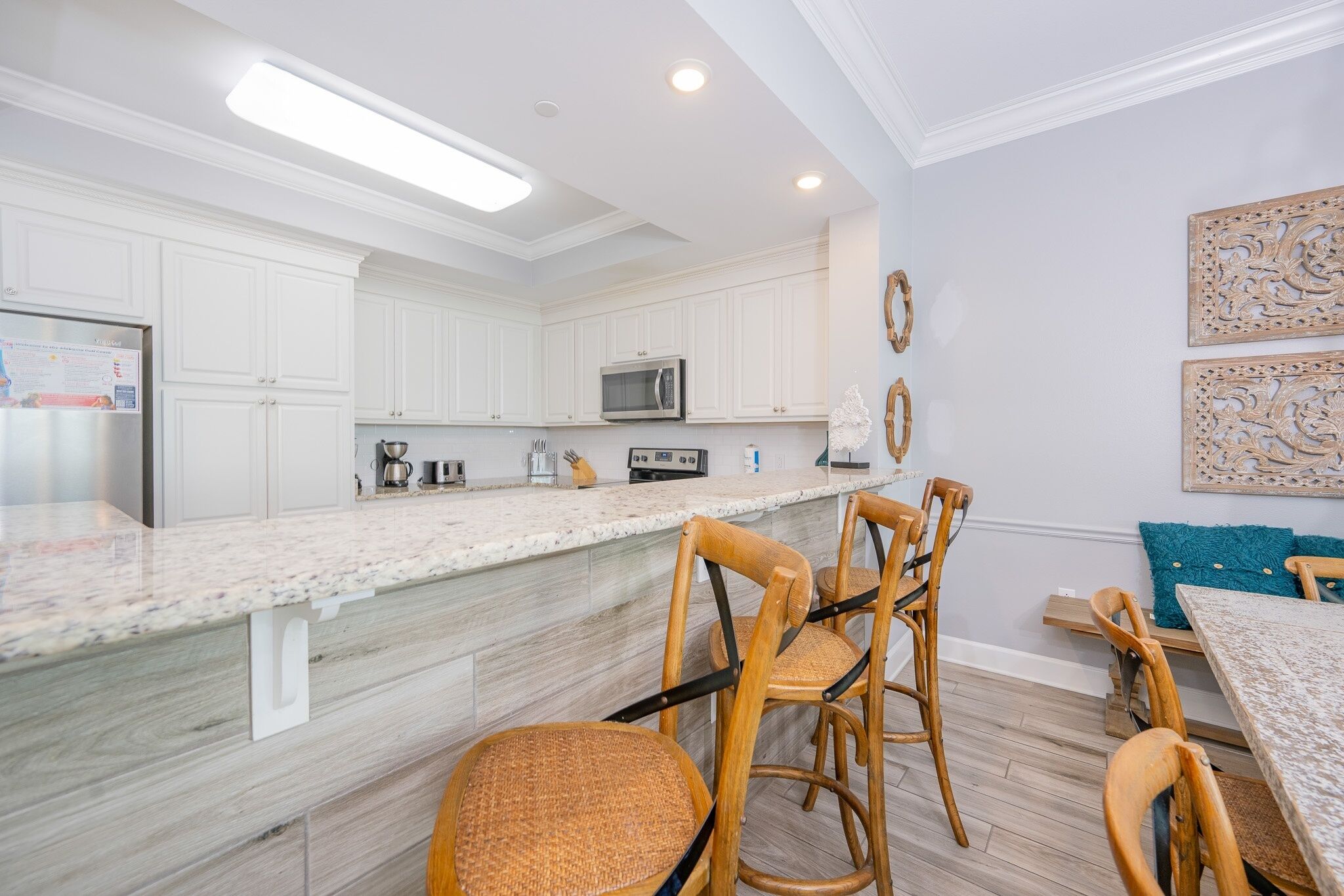 A modern kitchen with white cabinets, a granite countertop, and a dining area with wicker chairs and a wooden table.