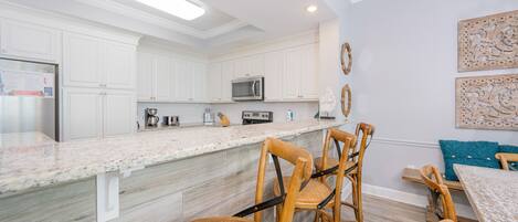 A modern kitchen with white cabinets, a granite countertop, and a dining area with wicker chairs and a wooden table.