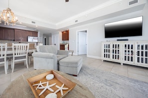 A spacious living room with a dining area, a large flat-screen TV, and a wooden coffee table with starfish. - Phoenix Gulf Shores by Brett/Robinson Vacations (Gulf Shores)