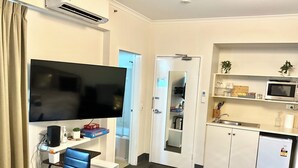 A compact hotel room with a flat-screen TV, a small kitchenette, a dining area with a table and chairs, and a door leading to a bathroom. - LOVELY ADELAIDE CITY ESCAPE (Adelaide)
