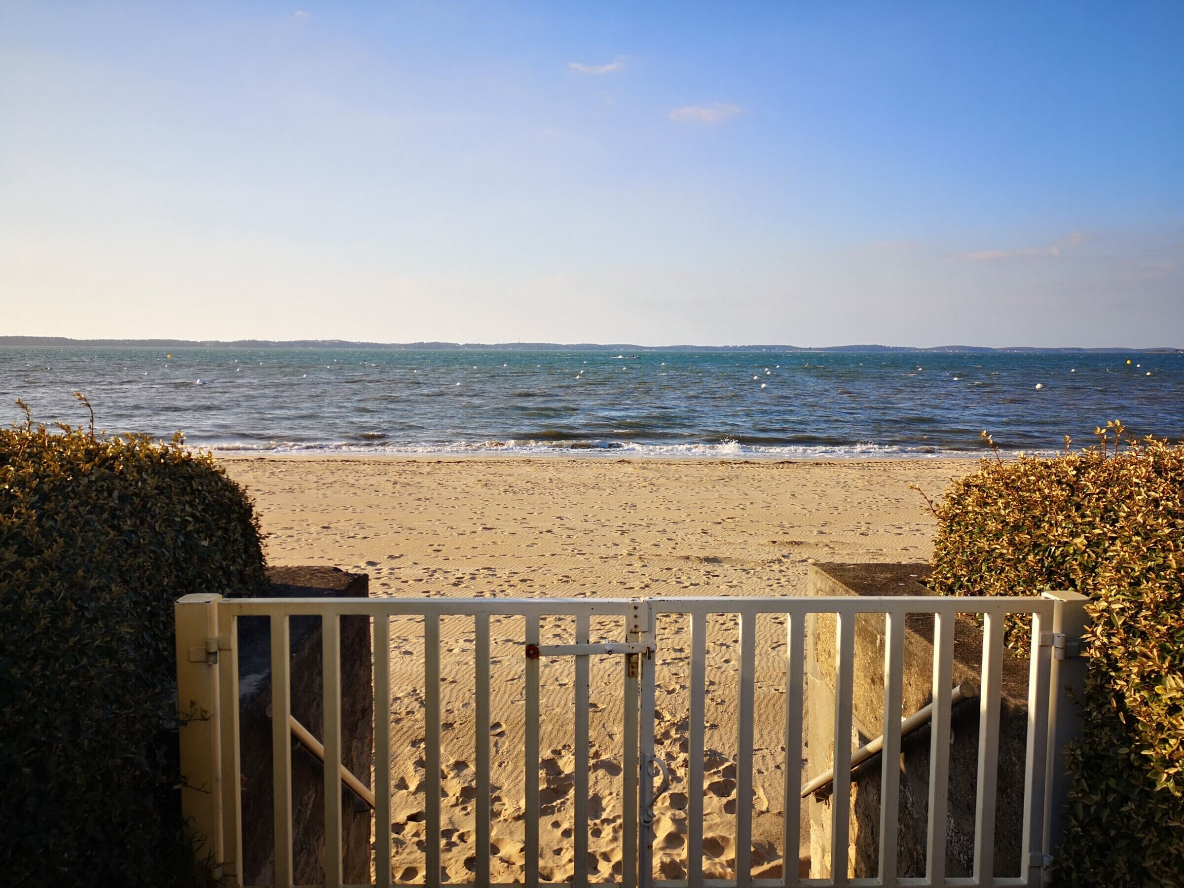 A beach with a sandy shore and a metal gate leading to the water.