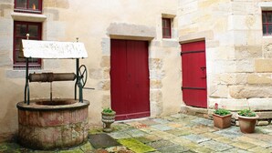 Un patio con un edificio de piedra, una puerta roja, una bomba de agua y plantas en macetas.