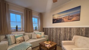 Un salon avec un canapé, un fauteuil, une table basse et un tableau accroché au mur.