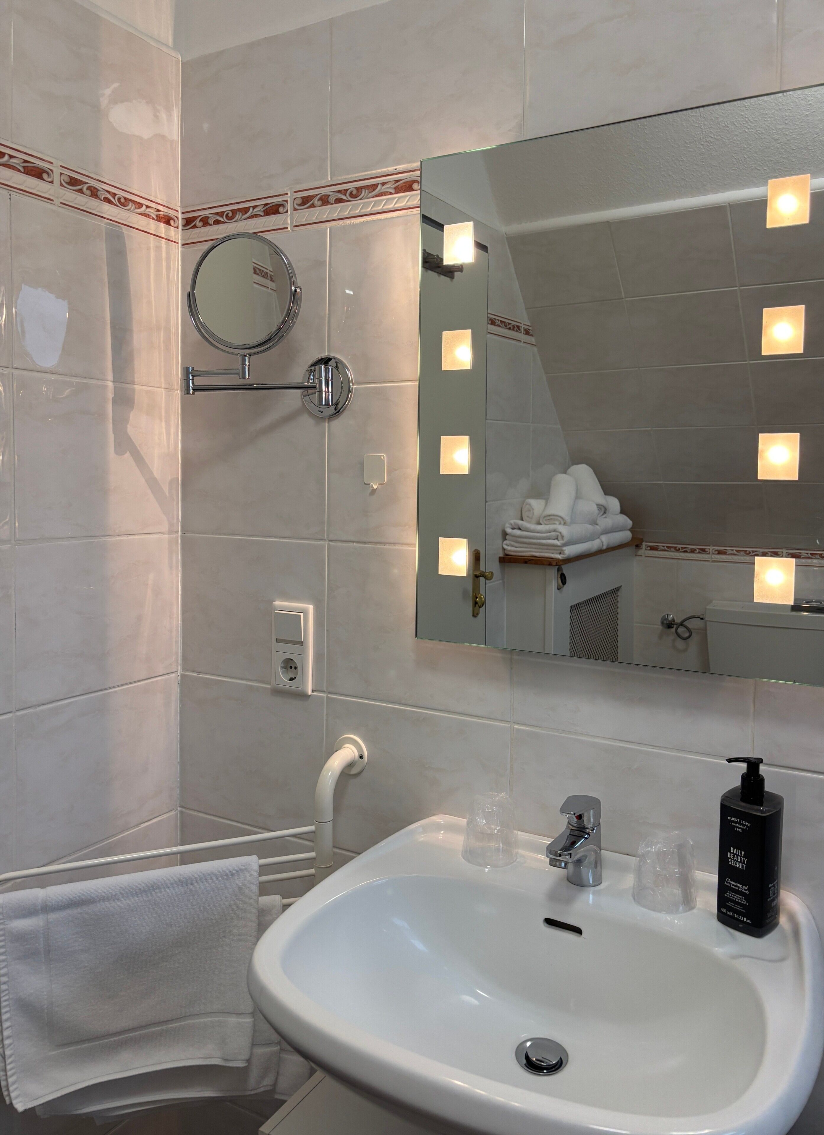 A bathroom with a sink, mirror, towel rack, and a shower area.