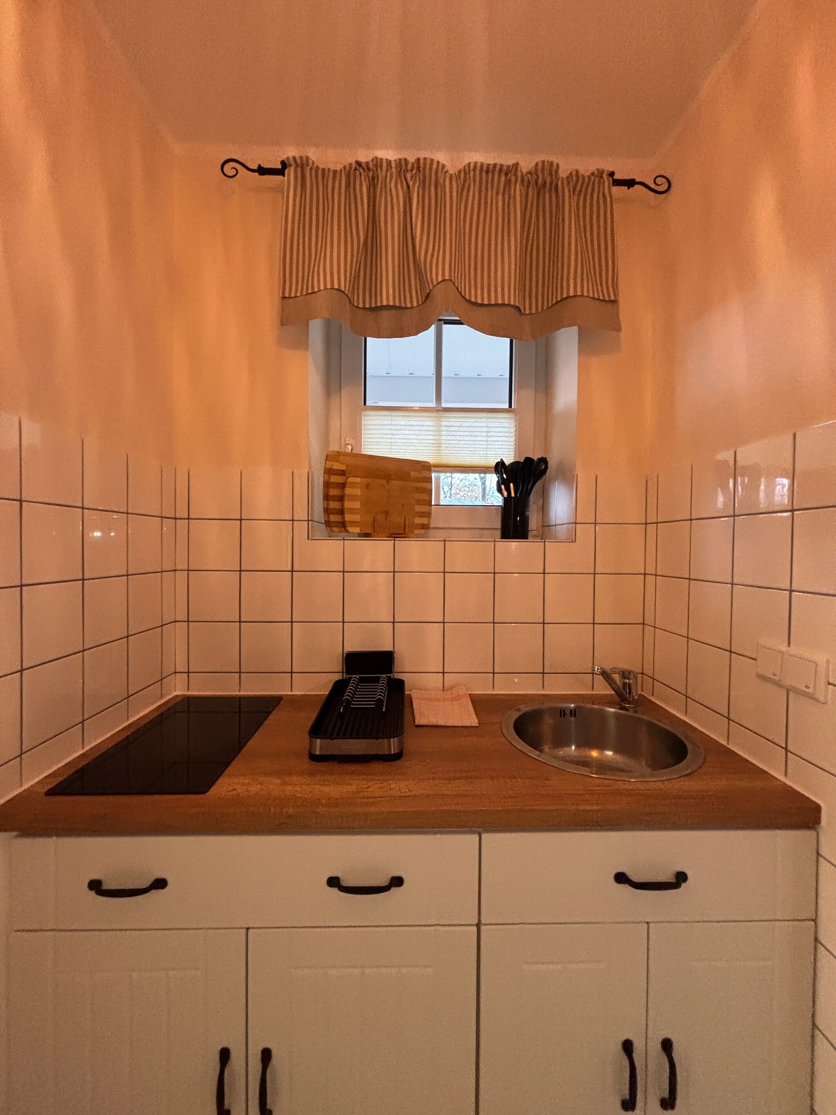 Una cocina compacta con ventana, un lavabo, una tabla de cortar y un portalápices para cuchillos.