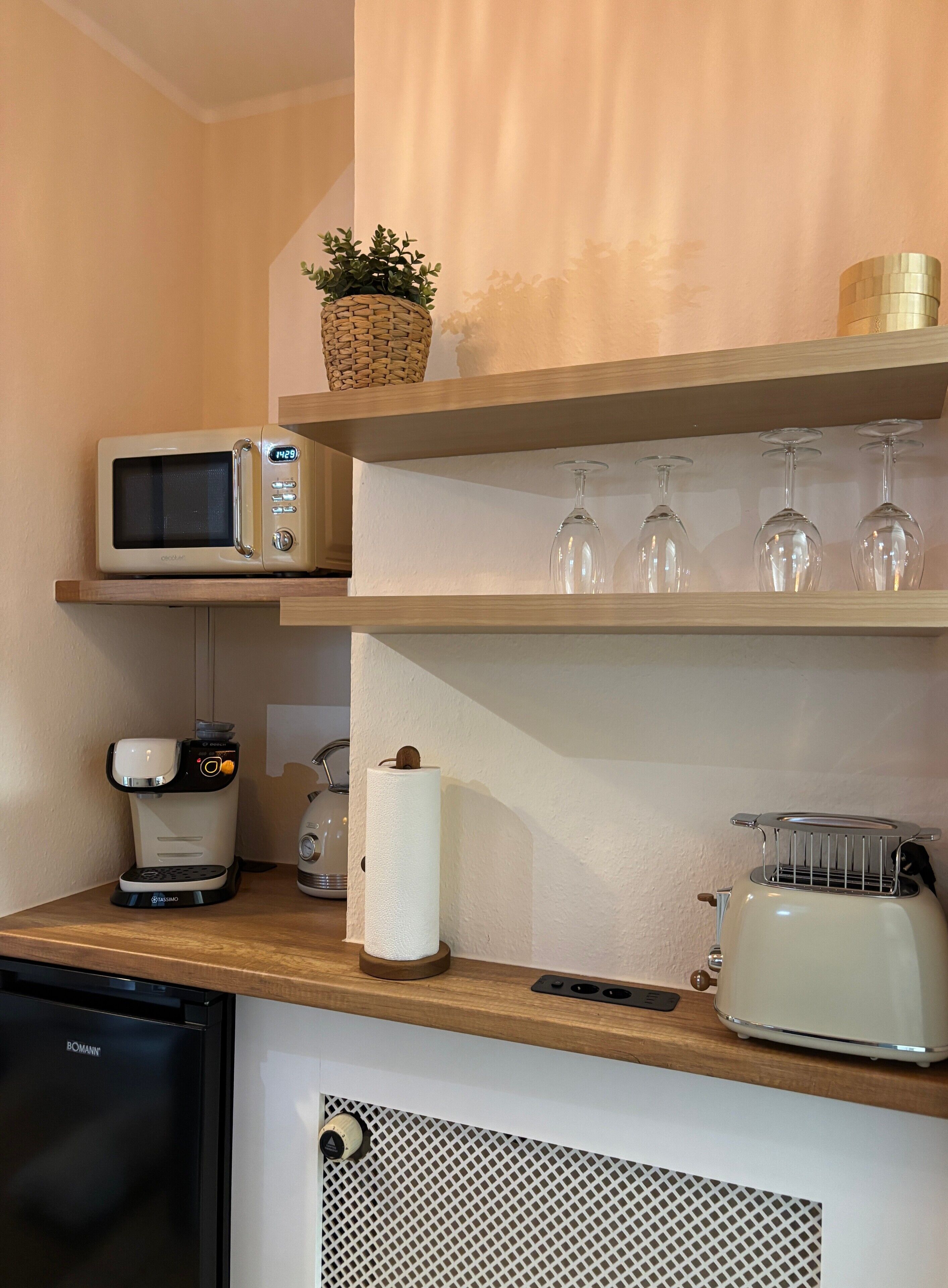 A kitchen with a microwave, coffee maker, toaster, and wine glasses on shelves.