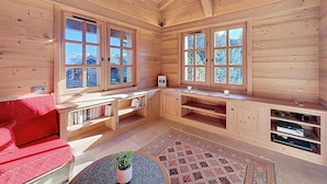 A wooden cabin interior with large windows, a red sofa, a small table with a plant, and built-in shelves. - Spacious 5-bedroom chalet near ski bus, Mont Blanc view (Combloux)