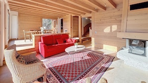 A spacious living area with a red sofa, wicker chairs, a patterned rug, and a fireplace. - Spacious 5-bedroom chalet near ski bus, Mont Blanc view (Combloux)