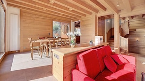 A spacious wooden cabin interior with a dining area, a red sofa, and a kitchen counter. - Spacious 5-bedroom chalet near ski bus, Mont Blanc view (Combloux)