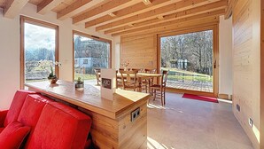 A wooden interior with a dining area, large windows, and a red chair. - Spacious 5-bedroom chalet near ski bus, Mont Blanc view (Combloux)