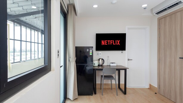Une chambre d’hôtel moderne dotée d’une grande fenêtre, d’un téléviseur à écran plat fixé au mur, d’une petite kitchenette et d’une armoire en bois.