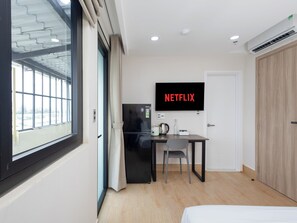 Una habitación de hotel moderna con un ventanal grande, un televisor de pantalla plana en la pared, una kitchenette pequeña y un armario de madera.