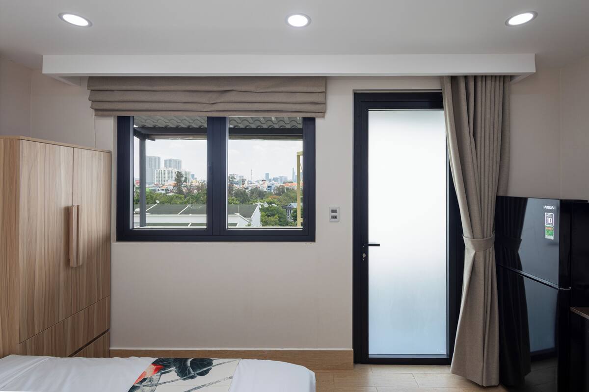 Ein modernes Hotelzimmer mit Bett, Schrank und Blick auf die Stadt durch ein großes Fenster.