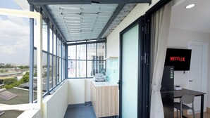 Un balcon donnant sur des immeubles, un petit bureau avec une chaise et un écran de télévision affichant le logo « NETFLIX ».