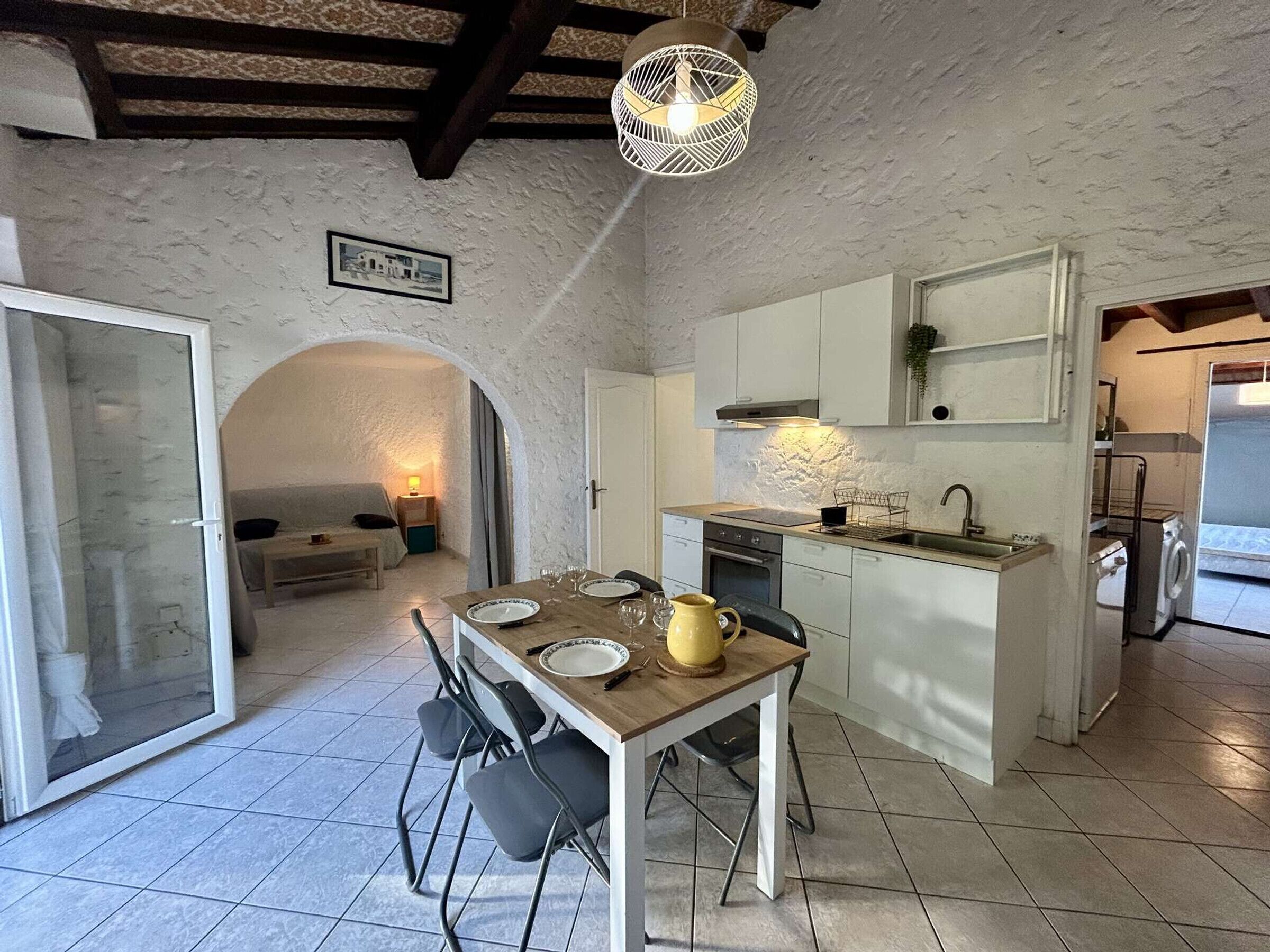 Een compacte keuken met een eethoek, met een betegelde vloer, een houten tafel met stoelen, een hangende lamp en een zichtbare oven.