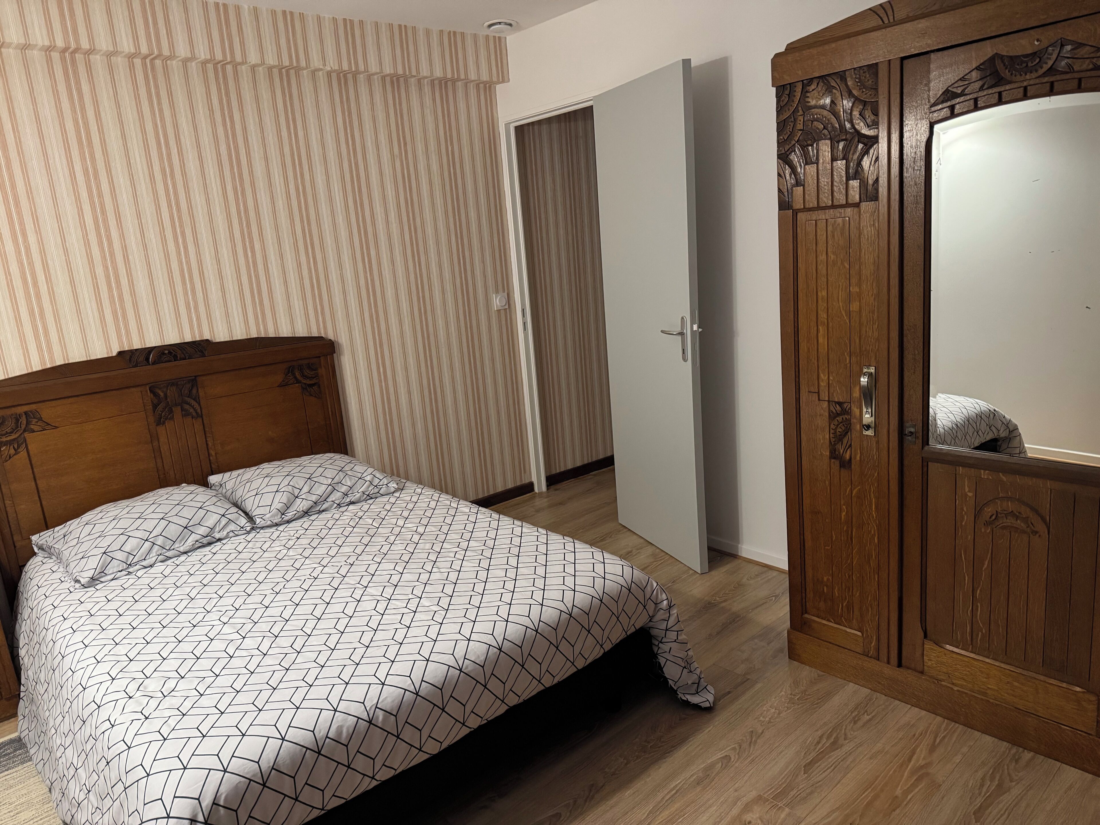 A bedroom with a wooden bed, a wardrobe, and a door leading to another room.