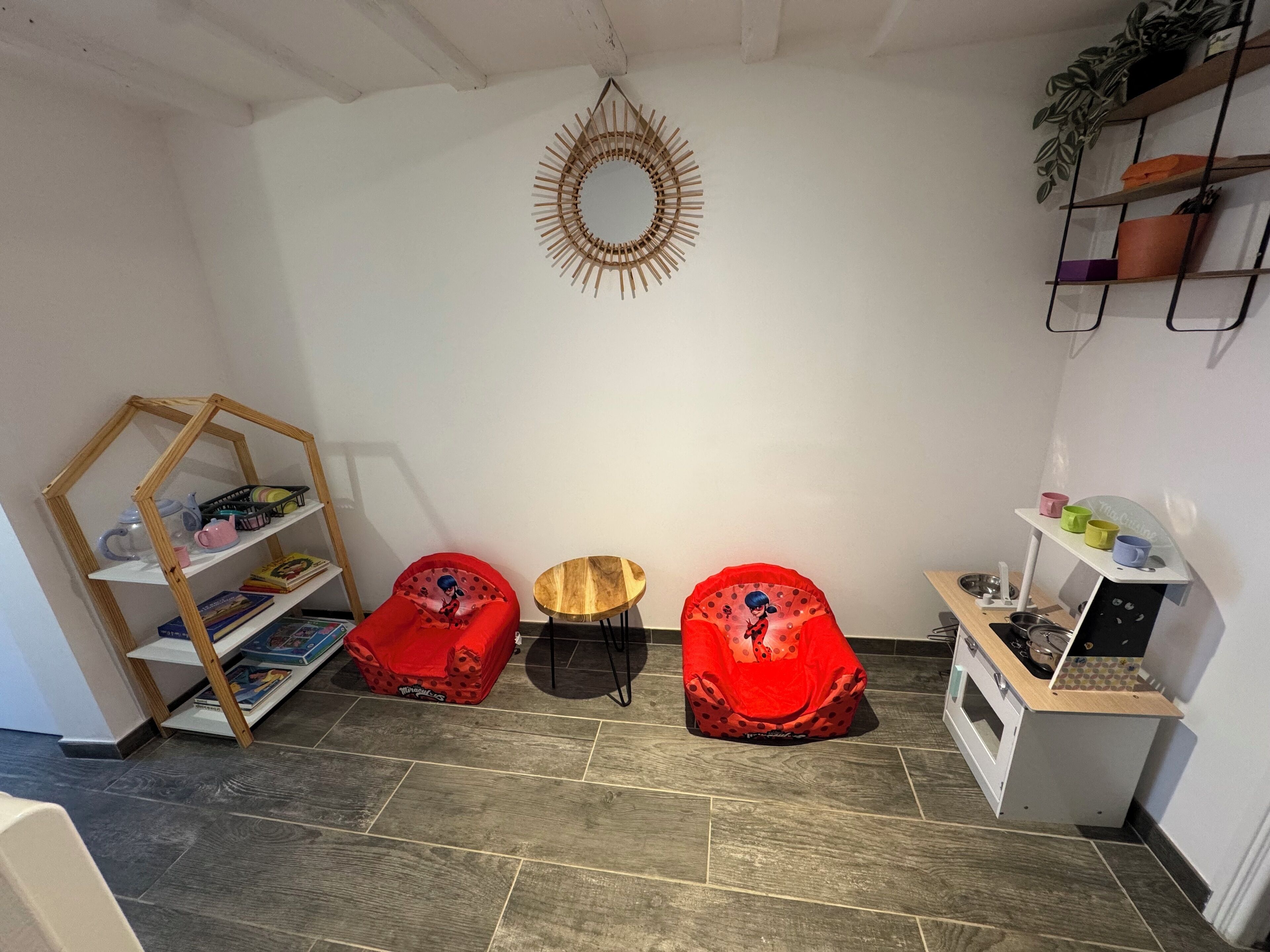 A cozy room with a wooden bookshelf, two red bean bags, a small round table, and a white cabinet with a sink.