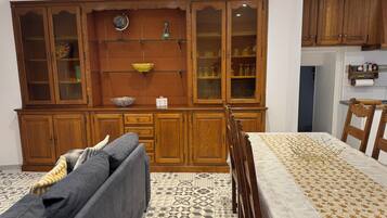 A dining area with a wooden cabinet, a table with a patterned tablecloth, and a sofa with cushions.