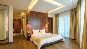 Habitación de hotel con una cama grande, paneles de madera, dos lámparas de pared, una mesita de noche con teléfono y una ventana con cortinas.