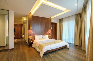 A hotel room with a large bed, wooden paneling, two wall-mounted lamps, a bedside table with a telephone, and a window with curtains.