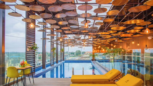 Un área de piscina interior moderna con vistas a la ciudad, sillas de descanso amarillas e iluminación circular en el techo.