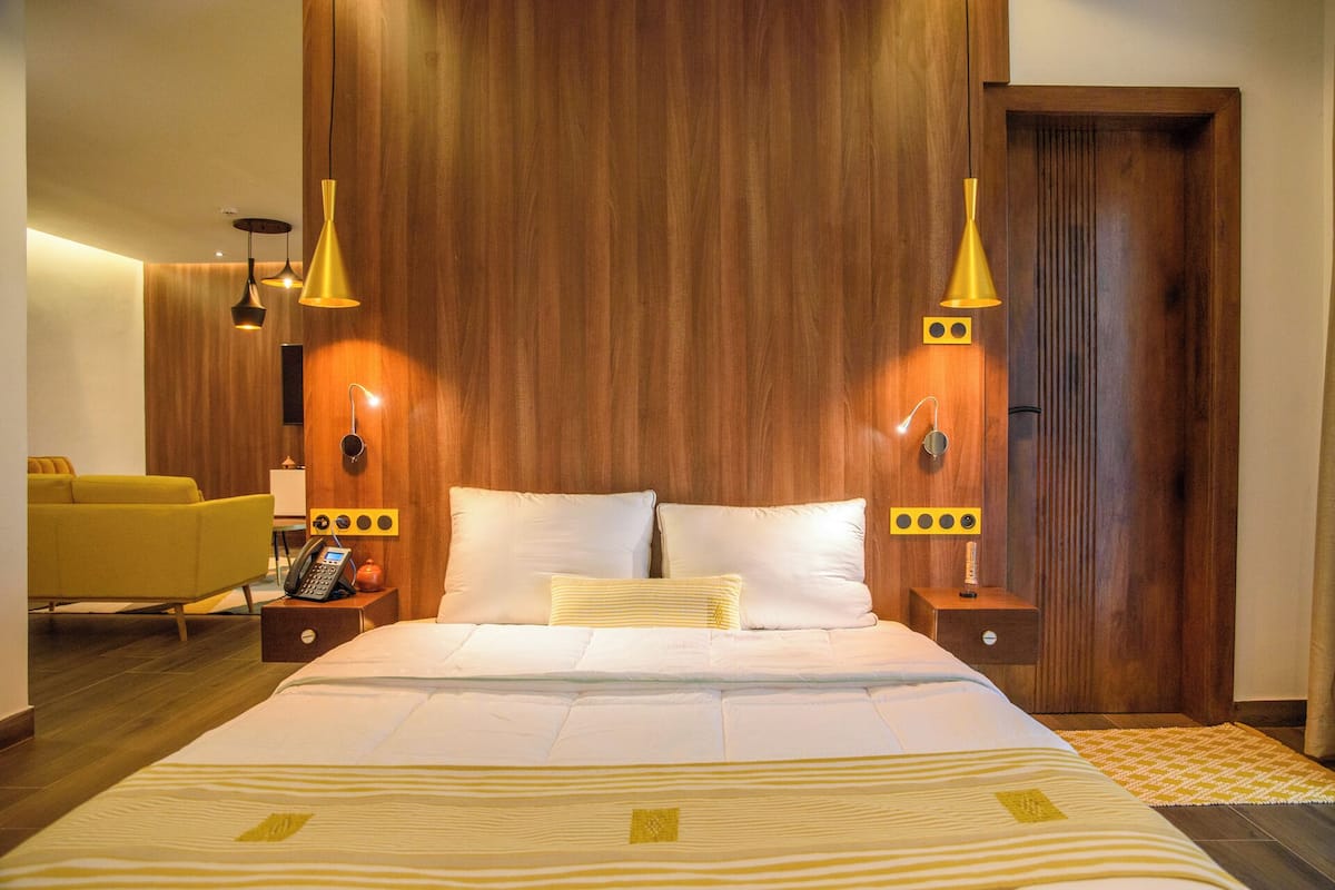 A hotel room with a large bed, wooden panel walls, two bedside tables with lamps, a sofa, and a TV.