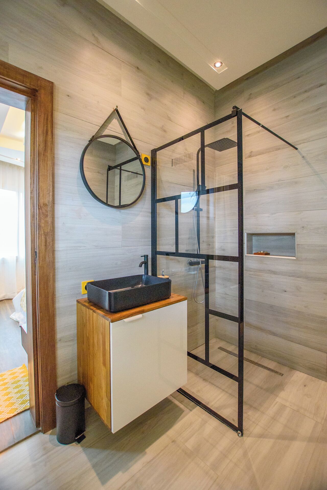 Une salle de bain moderne avec un meuble-lavabo en bois, un miroir rond et une cabine de douche en verre.