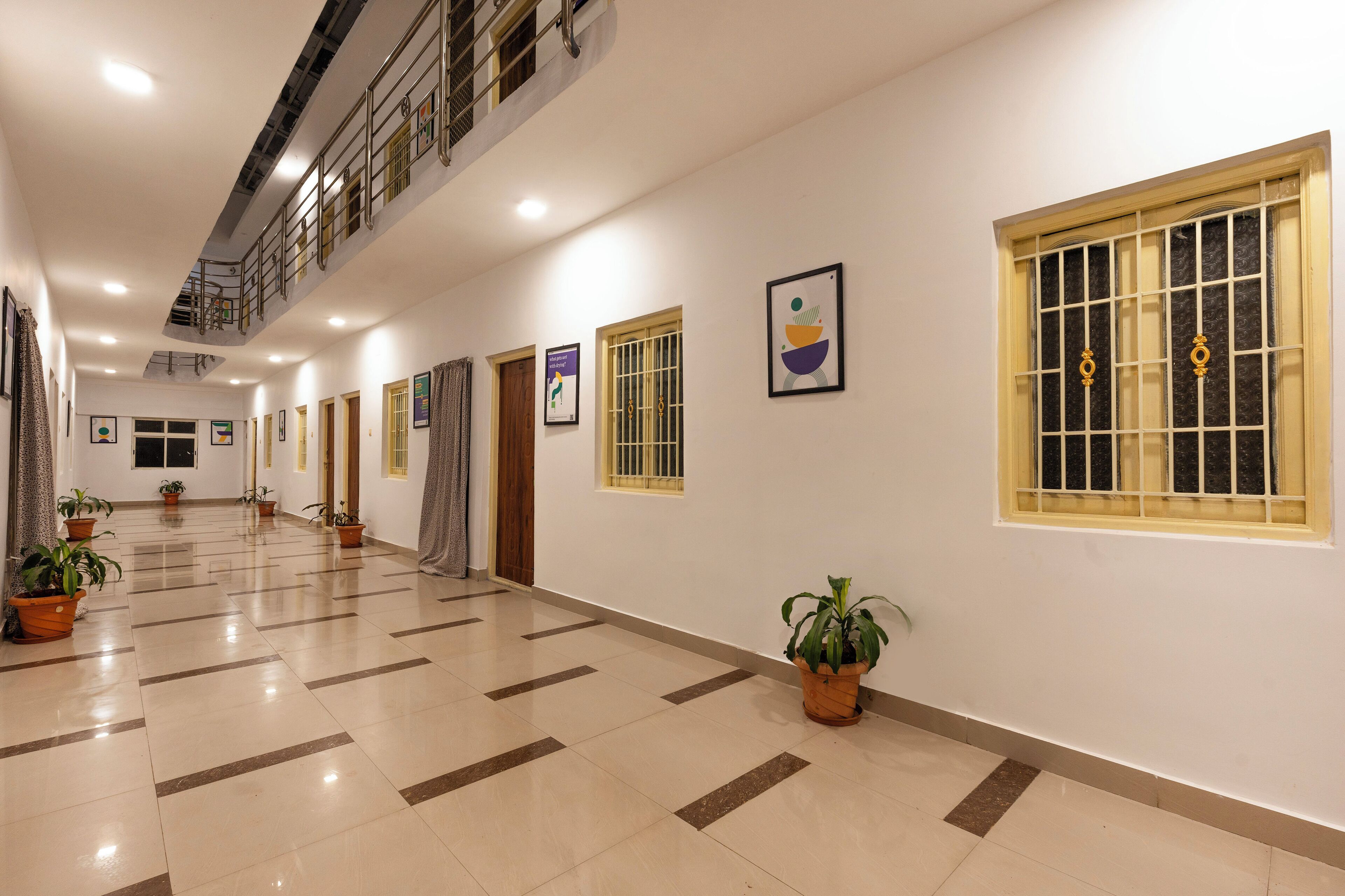 A long, well-lit corridor with tiled flooring, potted plants, and framed artwork on the walls.