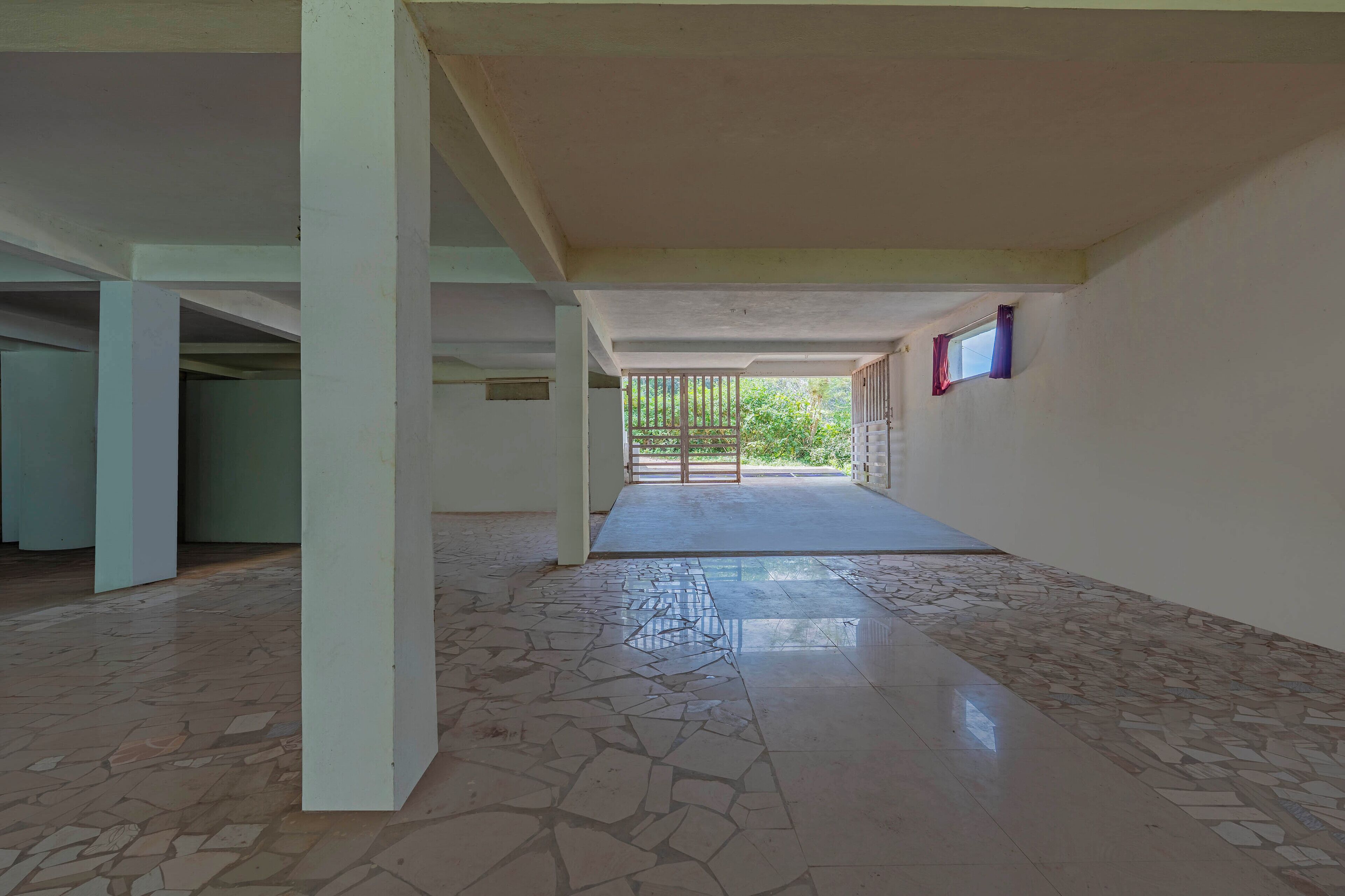 An empty corridor with tiled flooring, white walls, and a view of greenery outside.