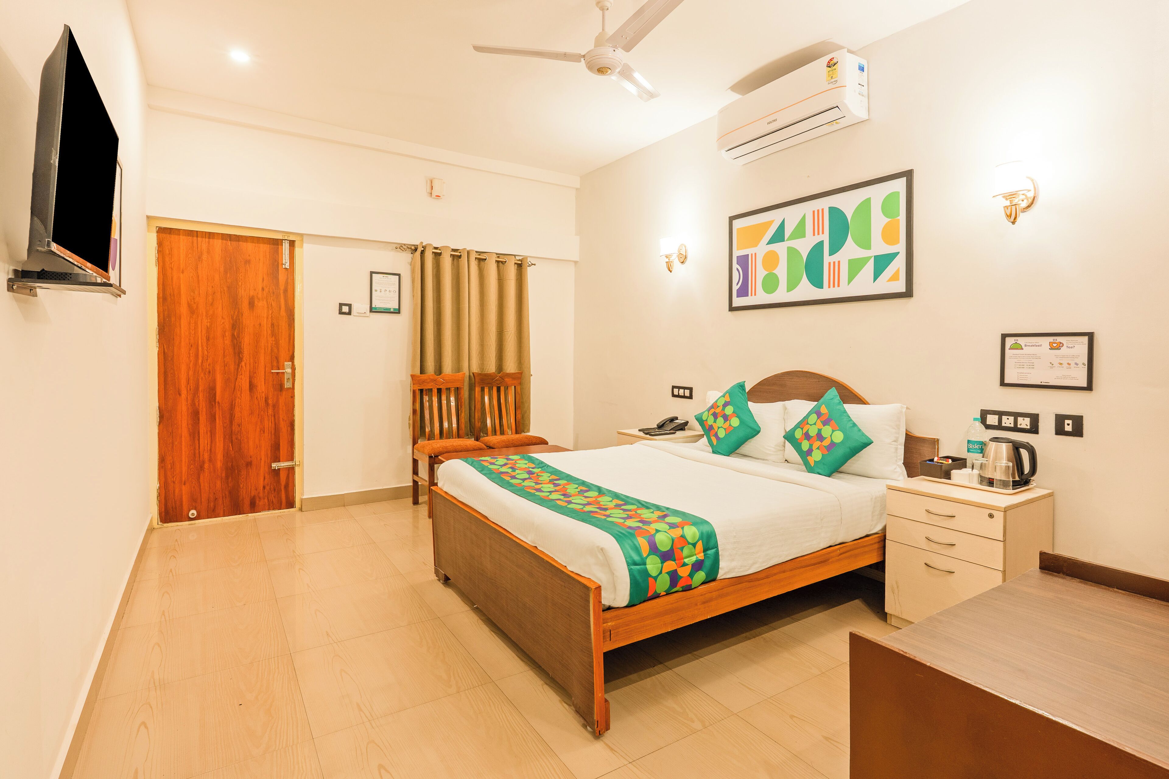 Une chambre d’hôtel avec un lit en bois, une table de chevet, un bureau, un ventilateur de plafond, un appareil de climatisation et un téléviseur.