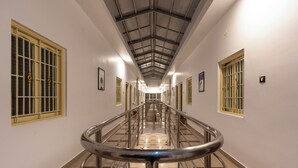 A long, narrow hallway with a central staircase, flanked by windows with metal bars and a high ceiling with a grid-like pattern. - Treebo Golden Paradise (Yercaud)