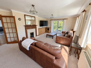 A living room with a brown leather sofa, a wooden coffee table, a fireplace, and a television. - Cae Erwyn - Coastal Escape with Hot Tub, Cinema & Games Room (Anglesey)