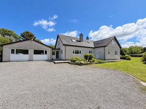 A two-story house with a gravel driveway, a garage, and a well-maintained lawn. - Cae Erwyn - Coastal Escape with Hot Tub, Cinema & Games Room (Anglesey)