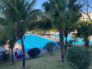 A swimming pool surrounded by palm trees and a grassy area with a fence. - Modern apartment with a full-service recreational area and access to the Golden Dolphin. (Caldas Novas)
