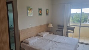 A hotel room with a large bed, a nightstand with a lamp, a chair, and a balcony with a view. - Modern apartment with complete leisure area and access to the Golden Dolphin. (Caldas Novas)