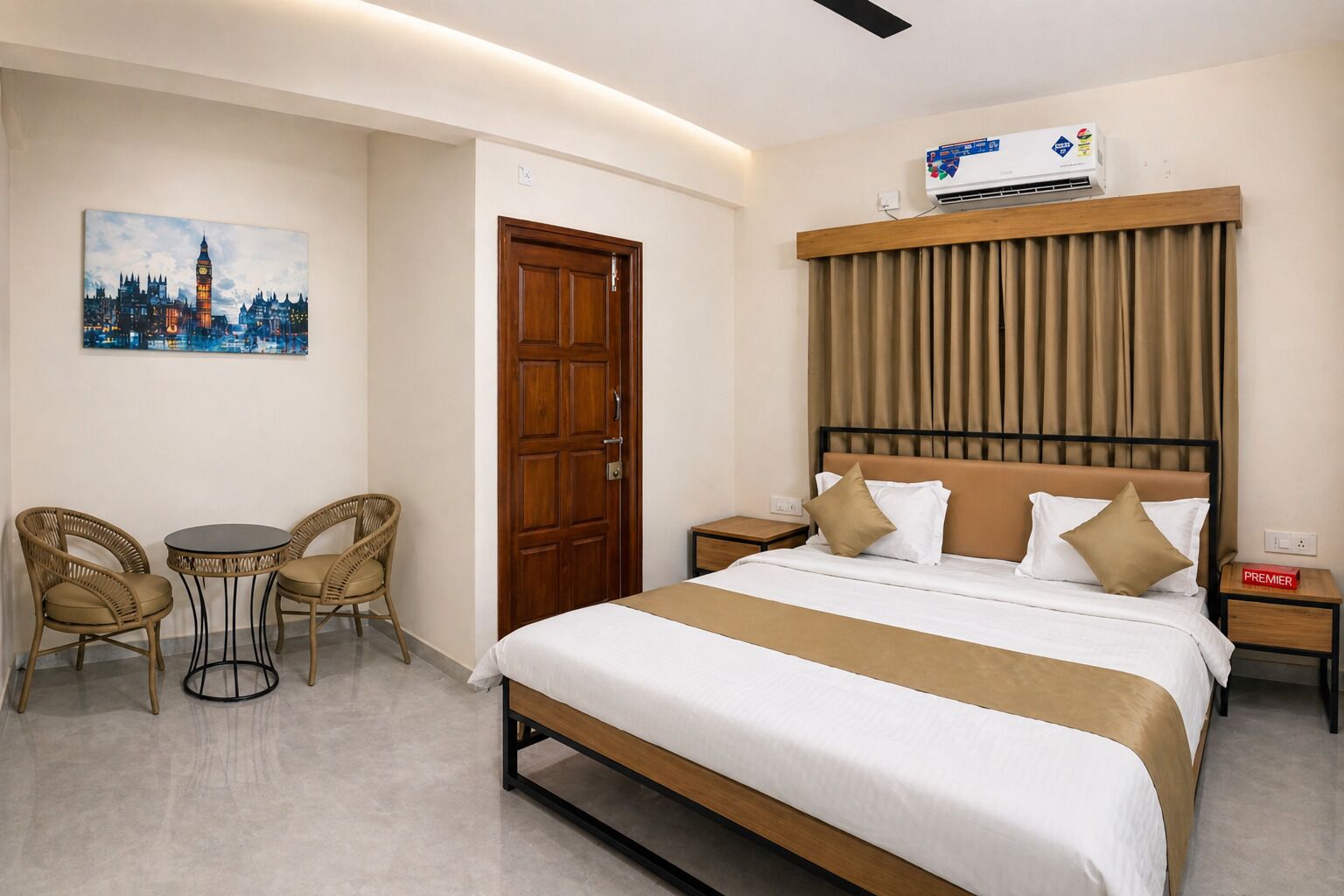 Une chambre d’hôtel comprenant un lit, une tête de lit en bois, une table de chevet, une table avec des chaises, un tableau représentant un paysage urbain et un appareil de climatisation.