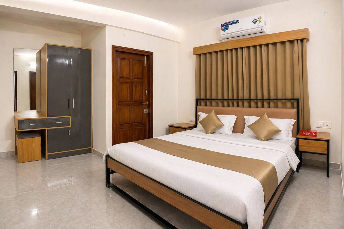 A hotel room with a bed, a wardrobe, a vanity, a nightstand, and an air conditioning unit.